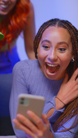 Close-Up-Vertical-Video-Studio-Shot-Of-Young-Gen-Z-Friends-Sitting-On-Sofa-Sharing-Social-Media-Post-On-Mobile-Phones-1